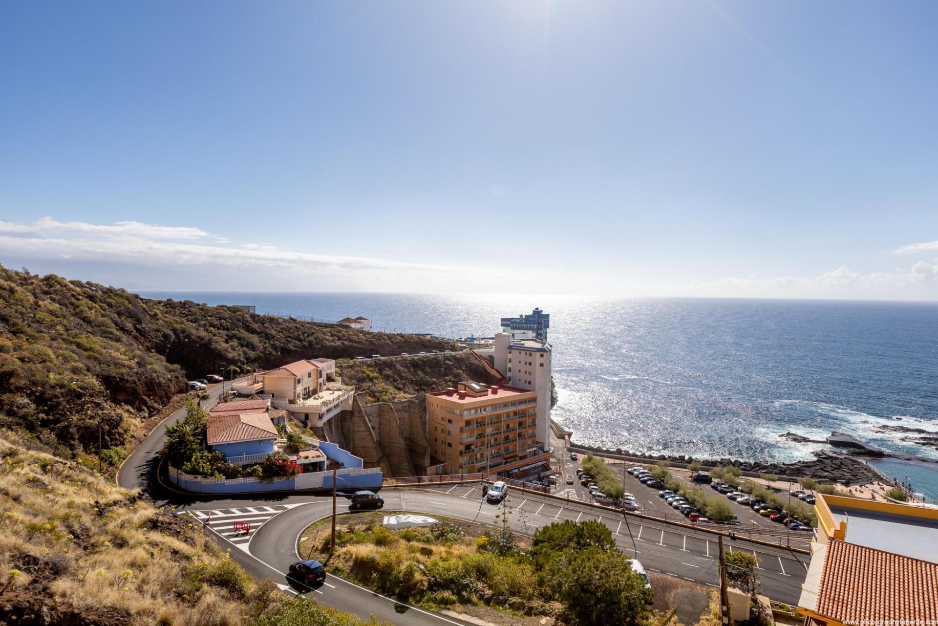 Vista amplia desde la terraza de una propiedad vacacional en Islas Canarias hacia el mar y el cielo azul, todo rodeado por vegetación verde abundante