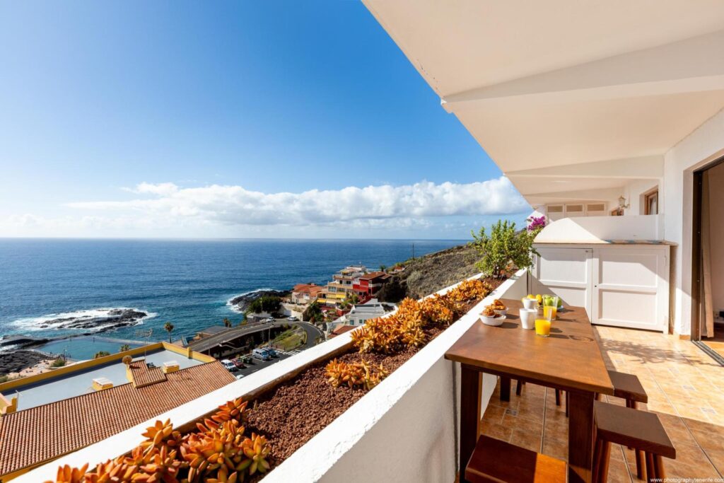 Terraza de apartamento vacacional con vista al mar, mesa de madera para compartir el desayuno, una vista increíble al mar azul y parte de Isla Canarias